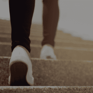 Une personne montant les escaliers, vue de derrière, avec des chaussures blanches et un éclairage doux.