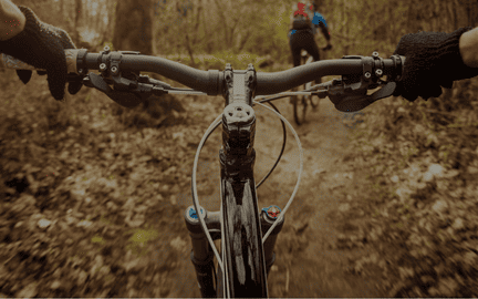 Vue à la première personne de la conduite d'un vélo sur un sentier forestier, avec des mains sur les poignées.
