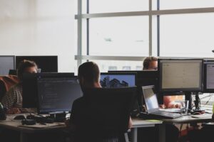 Bureau d'entreprise avec plusieurs personnes travaillant sur des ordinateurs, concentrées sur des écrans de code et de données.