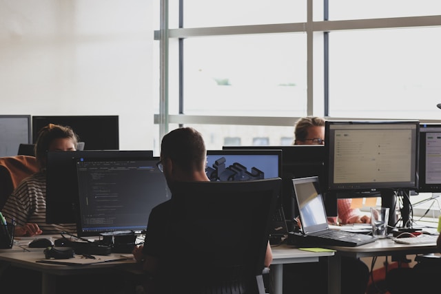 Bureau d'entreprise avec plusieurs personnes travaillant sur des ordinateurs, concentrées sur des écrans de code et de données.