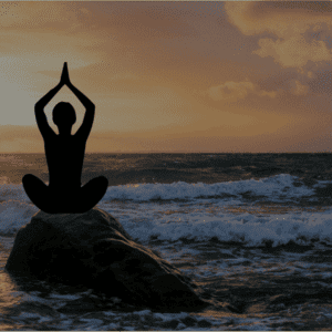 Silhouette d'une personne en méditation sur une roche, face à la mer, avec un coucher de soleil en arrière-plan.