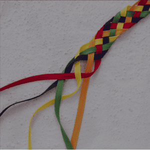 Des bandes de tissu colorées tressées, formant un motif multicolore de rouge, vert, jaune, bleu et orange sur un fond blanc.