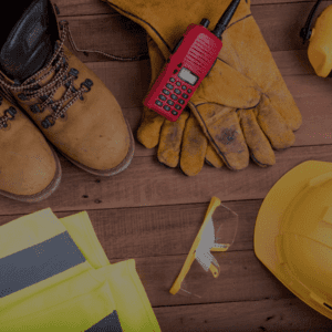 Des équipements de sécurité de chantier : bottes, gants, casque, radio et vêtements haute visibilité posés sur une surface en bois.