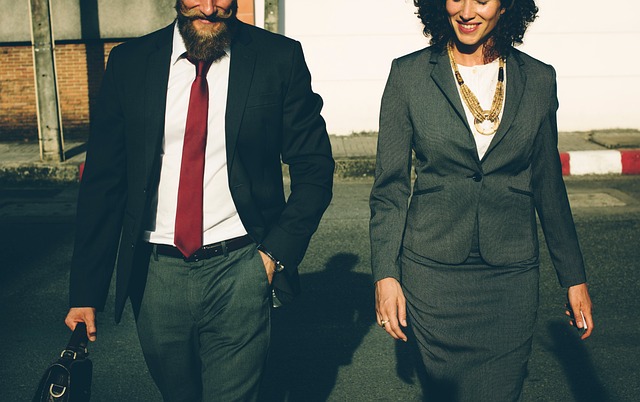 Un homme en cravate rouge et mallette noire marche aux côtés d’une femme en tailleur gris, reflétant collaboration et réussite urbaine.