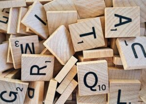 Un amas de tuiles en bois pour jeux de lettres, avec lettres noires et valeurs en points, symbolisant créativité, jeu intellectuel et vocabulaire.