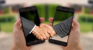 Deux mains serrant un accord, apparaissant à travers deux smartphones, symbolisant un partenariat numérique ou virtuel.