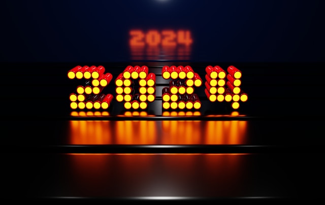 Le chiffre 2024 en LED orange vif, formé de points lumineux, brille sur un fond sombre avec un reflet moderne et futuriste.
