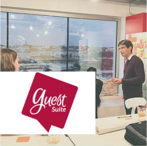 Mathieu anime une réunion dans une salle lumineuse avec vue urbaine, des post-it aux murs et le logo 'Guest Suite' au premier plan.